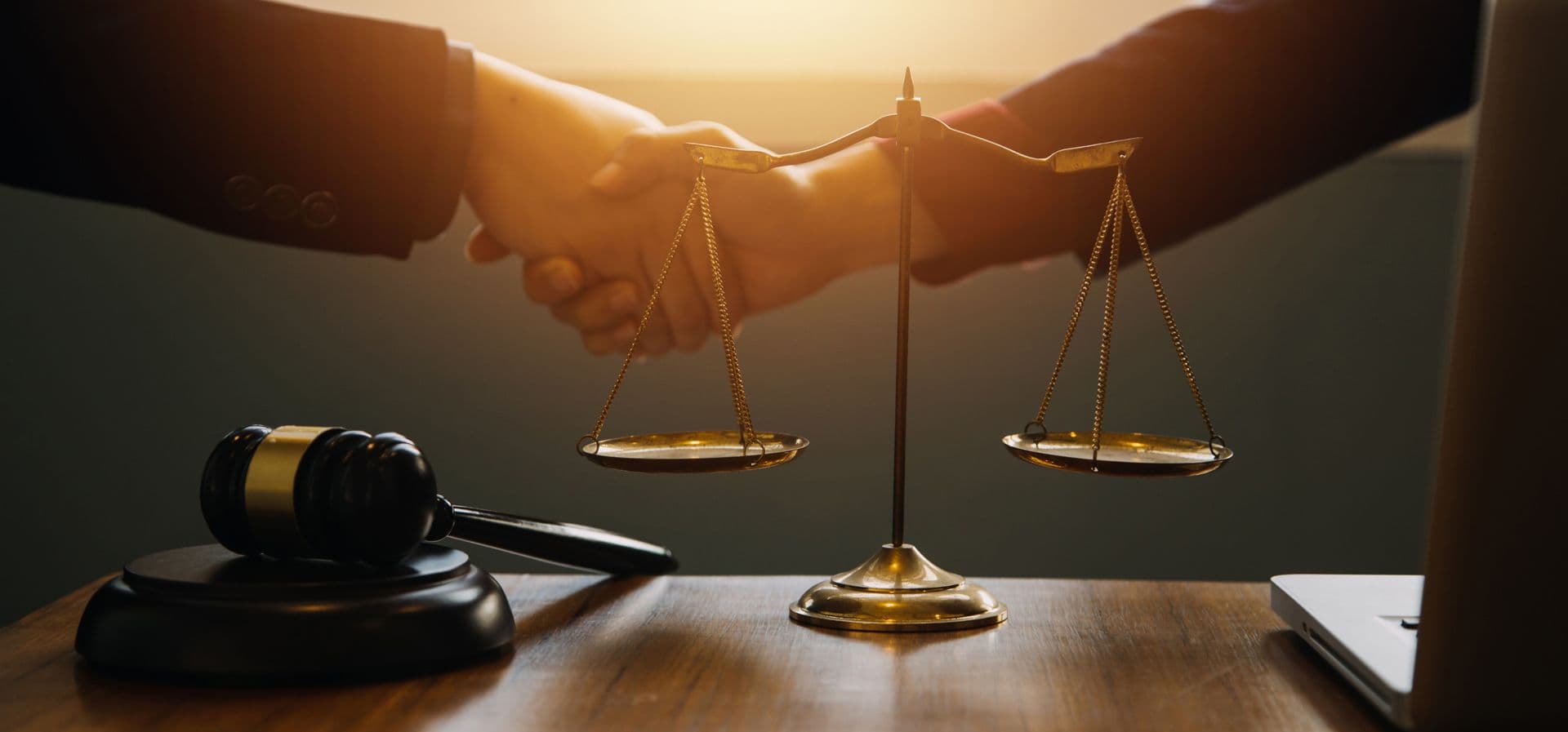 A handshake beside the scales of justice and a gavel on a desk